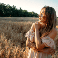 A woman in a light dress standing in a golden field during sunset, representing outdoor physical activity and wellness.