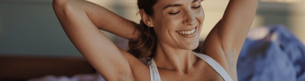 A woman smiling and stretching her arms, representing relief from pain through sports medicine and pain management services.