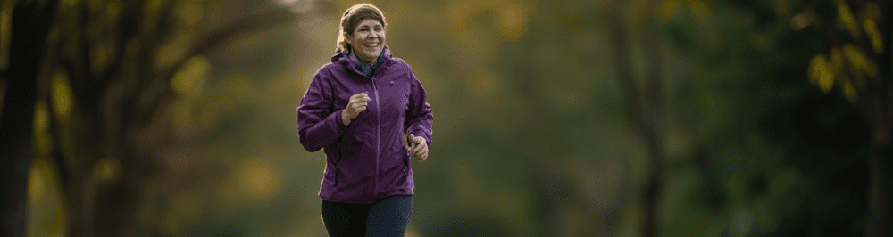 Woman jogging outdoors in fall scenery at Performance Pain and Sports Medicine clinic, specializing in sports injury treatment and pain management.