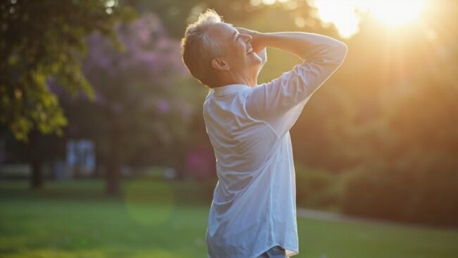 Relaxed middle-aged man enjoying sunny outdoor park, sports medicine, pain management, physical therapy, sports injury recovery, healthy aging, fitness, outdoor exercise, wellness, pain relief, performance improvement.