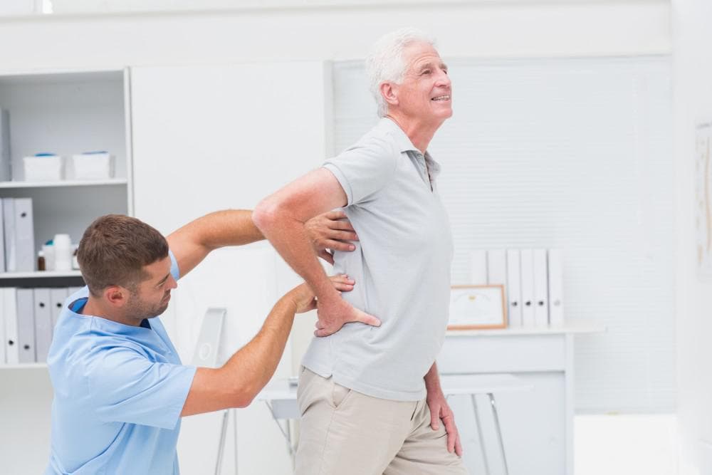 Chiropractic treatment for senior man with back pain at healthcare clinic.