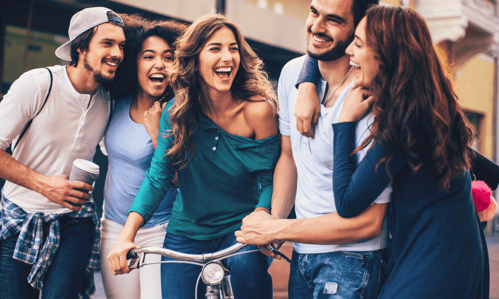 Smiling group of young adults laughter outdoor socializing, representing community and wellness at Performance Pain and Sports Medicine clinic for injury recovery and pain management.